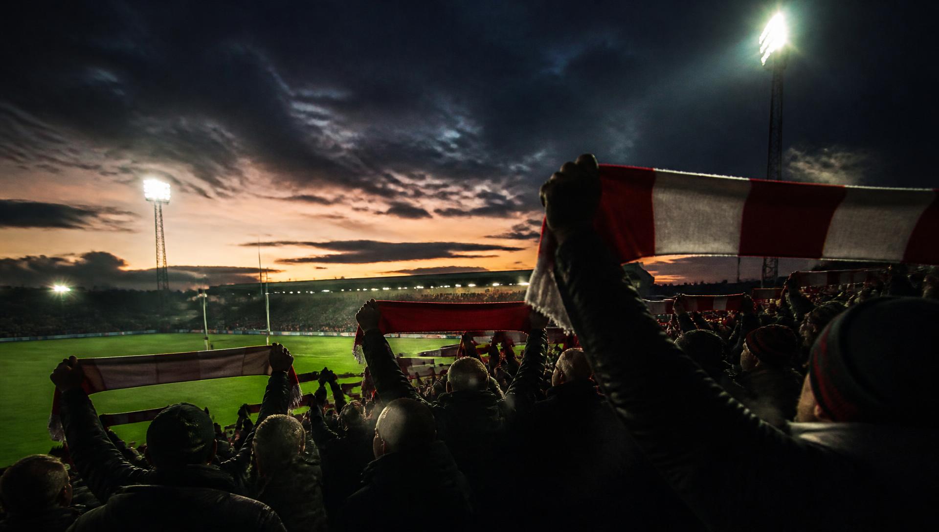 Oldham RLFC supporters raising scarves on a floodlit terrace